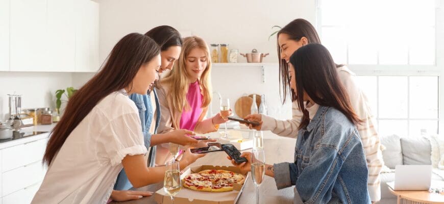 Five women gathered around a kitchen island and sharing a pizza